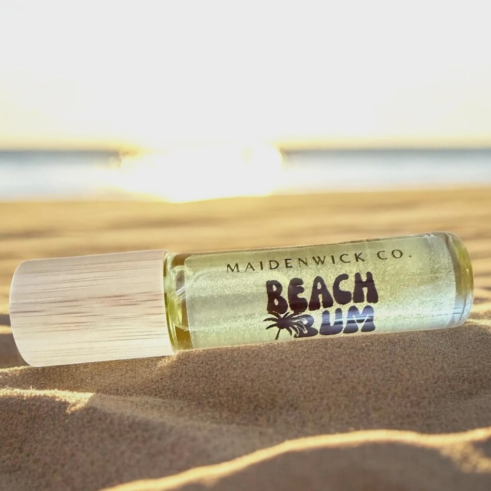 Beach Bum jojoba perfume oil roll-on resting on warm sand at sunset