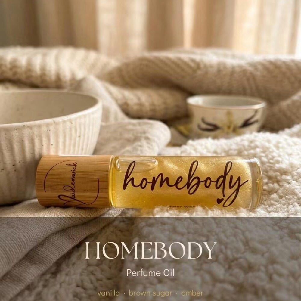 Homebody perfume oil roll-on with a wooden cap, styled on a soft cream knit